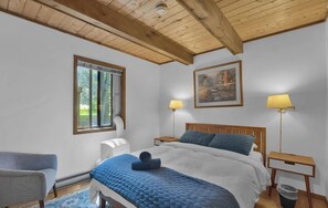 A bedroom with a bed, two bedside lamps, a window, a painting, and a chair.