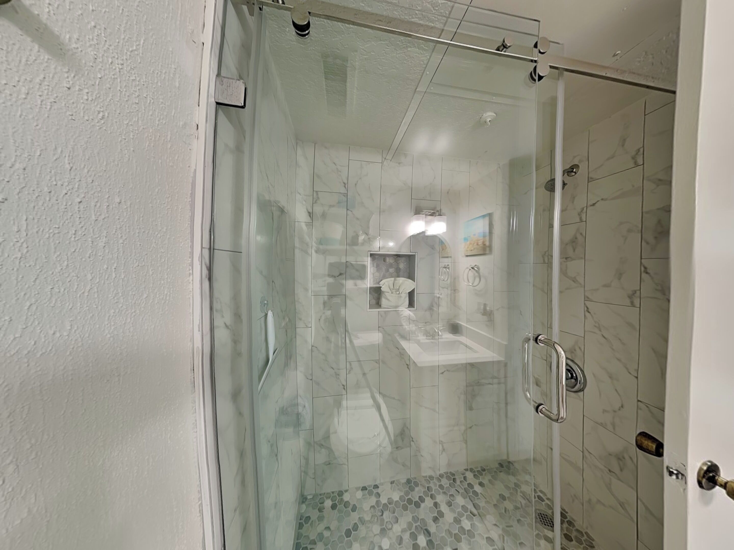 A modern bathroom with a glass-enclosed shower, a white sink, and a marble-tiled shower area.
