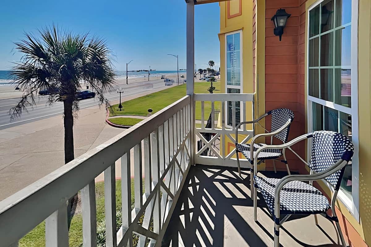 A balcony with two chairs, a palm tree, and a view of the beach and ocean.