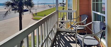 A balcony with two chairs, a palm tree, and a view of the beach and ocean.