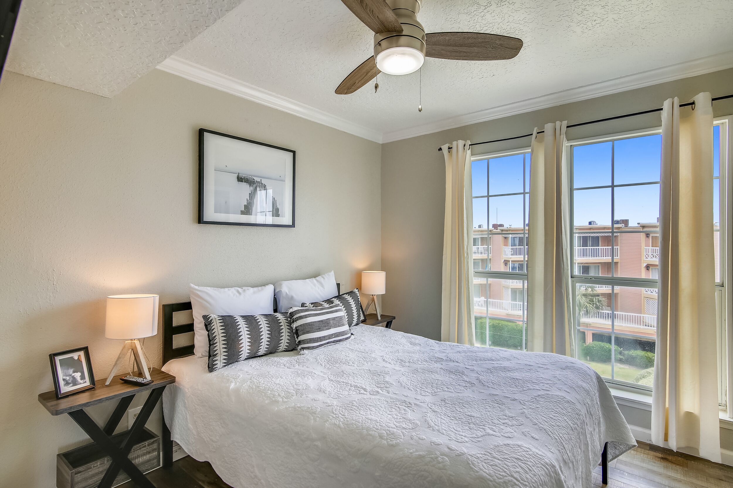 A neatly arranged bedroom with a large bed, a ceiling fan, and a window with curtains.