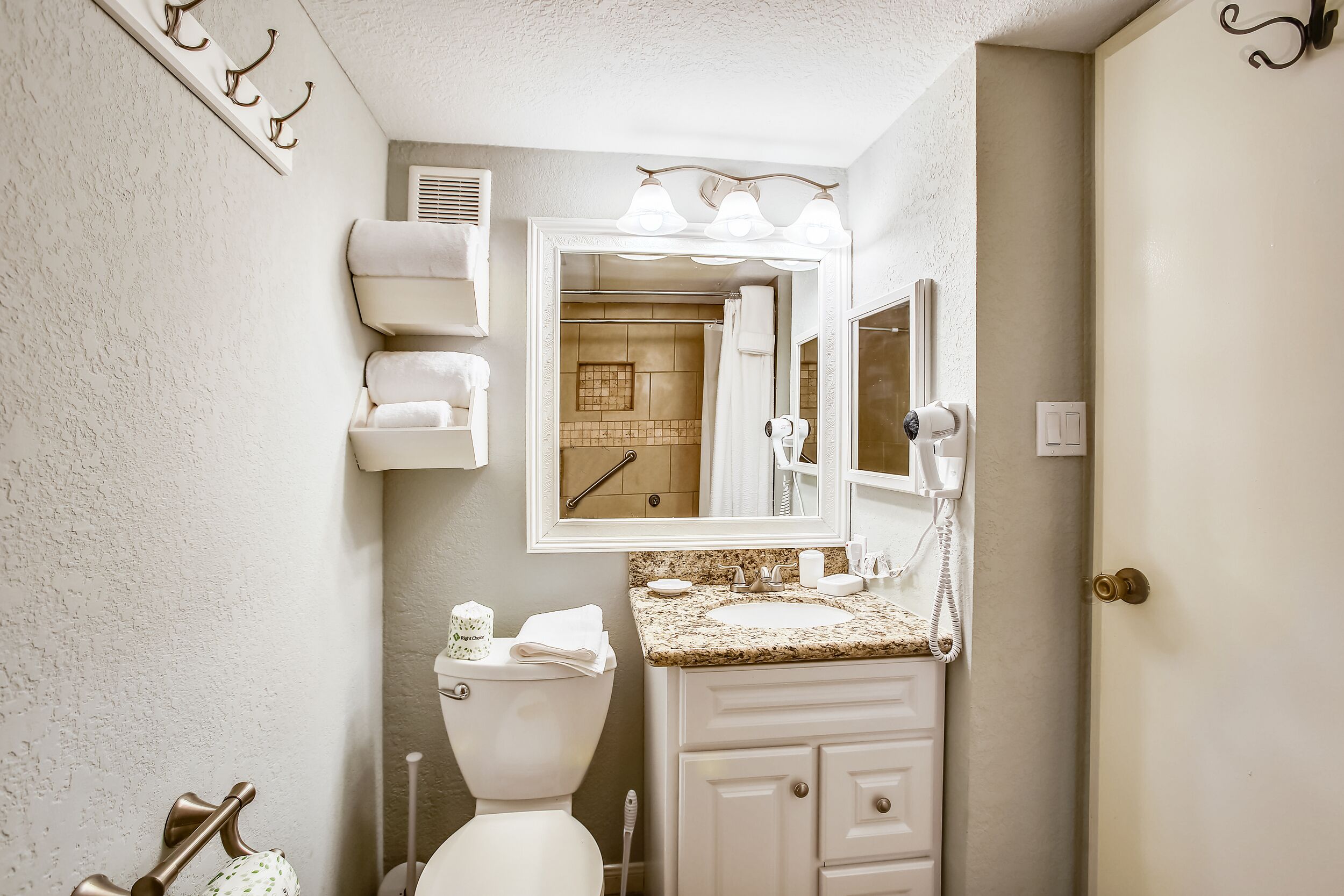A bathroom with a toilet, sink, and mirror. There are towels hanging on the wall and a shower visible in the background.