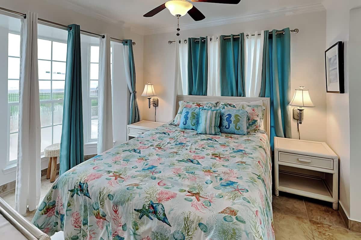 A bedroom with a bed, two bedside tables, a ceiling fan, and a window with curtains.