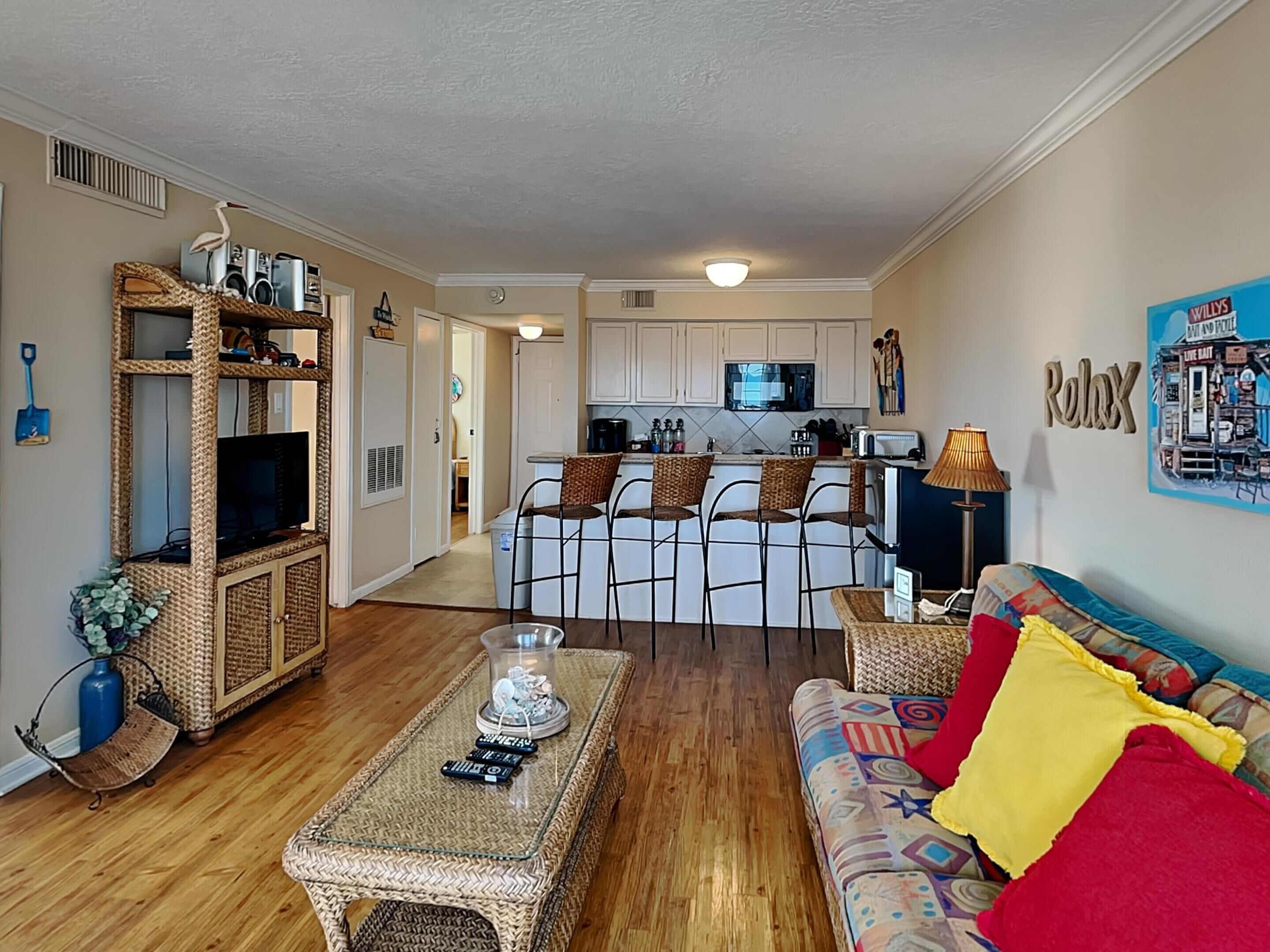 A cozy living room with a sofa, a coffee table, and a TV. There's a kitchen in the background with a dining area.