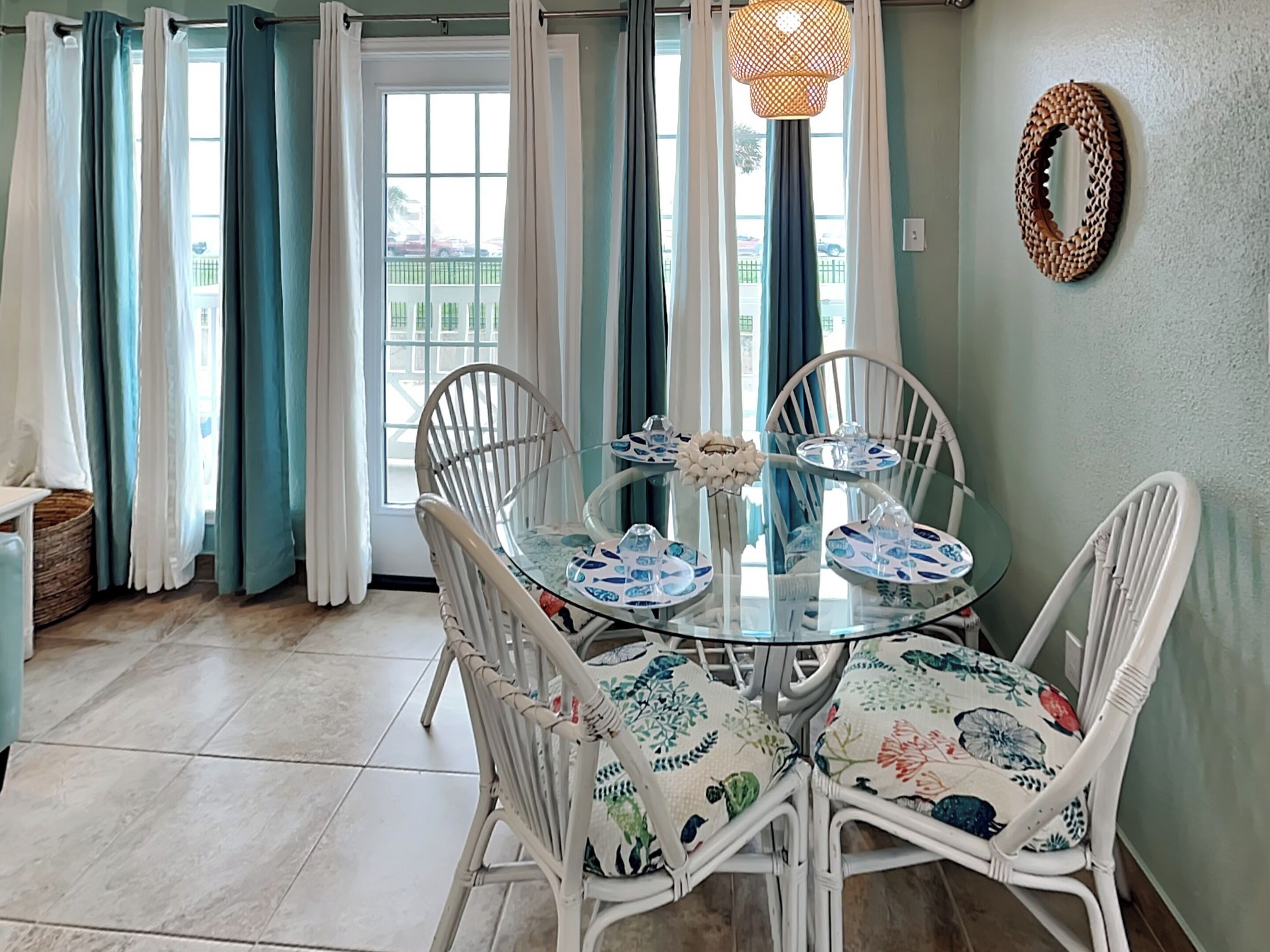 A dining area with a round glass table, white wicker chairs, and a woven light fixture.