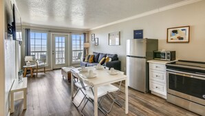 A compact kitchen with a dining area, a refrigerator, microwave, and a stove. - The Victorian by Ryson Vacation Rentals (Galveston)