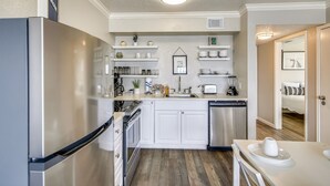 A compact kitchen with white cabinets, a stainless steel refrigerator, and a dishwasher. - The Victorian by Ryson Vacation Rentals (Galveston)
