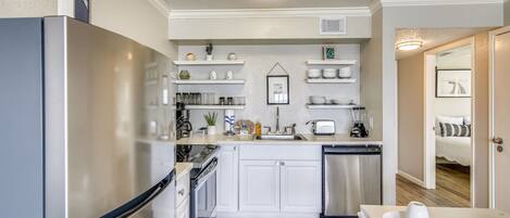 A compact kitchen with white cabinets, a stainless steel refrigerator, and a dishwasher.