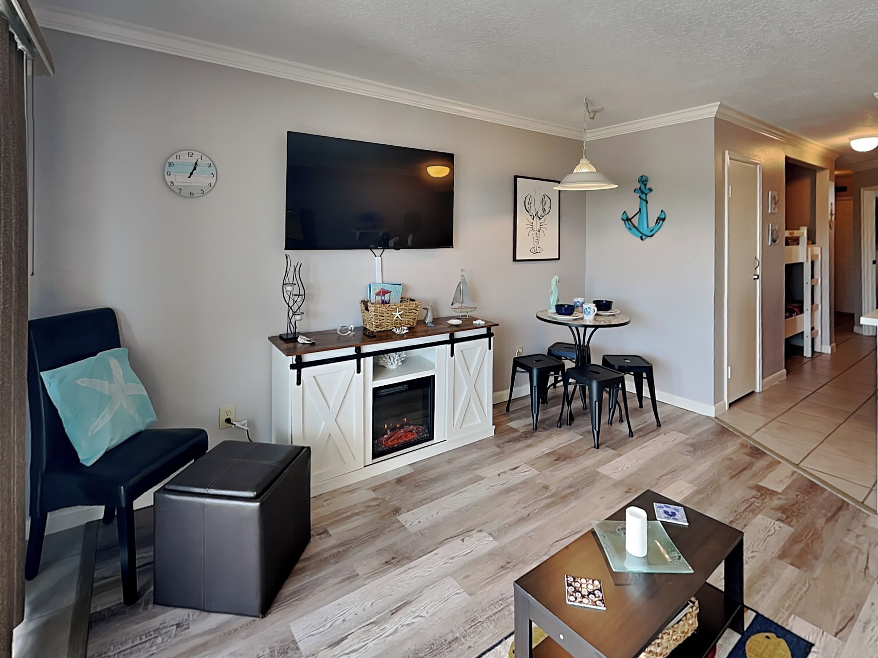 A living room with a fireplace, a dining area with a table and chairs, a TV mounted on the wall, and a hallway leading to another room.