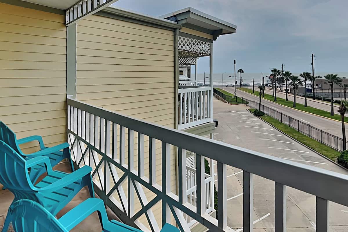 A balcony with turquoise chairs and a view of the beach and road.