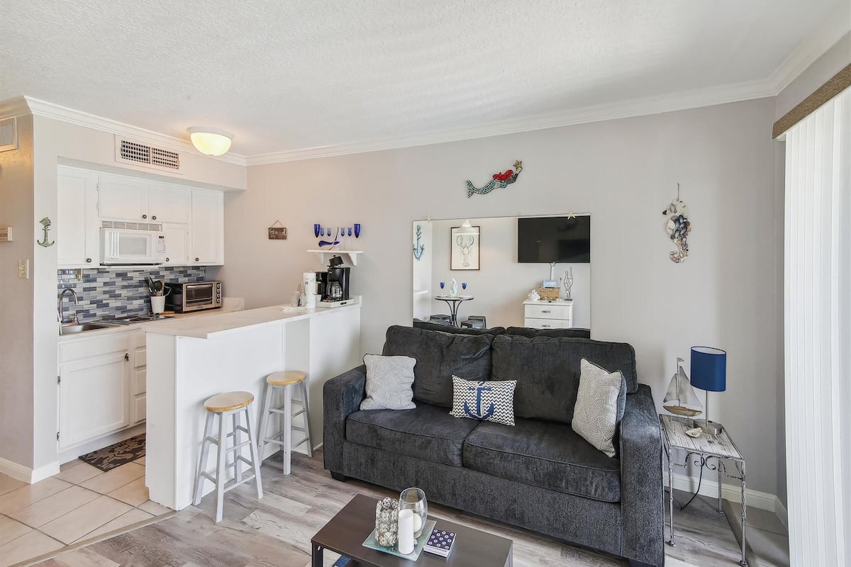 A compact living space with a kitchenette, a grey sofa, and a small dining area.
