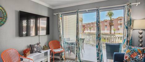 Una sala de estar moderna con una televisión, dos sillones naranjas, un sofá azul y un balcón con vistas a edificios.