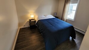Pieni, siististi järjestetty makuuhuone, jossa on yksi sänky, yöpöytälamppu ja yöpöytä.