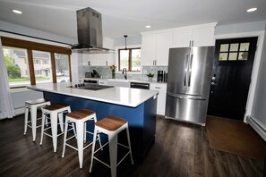 Een moderne keuken met een centraal eiland, barkrukken, roestvrijstalen apparatuur en uitzicht op de omgeving.