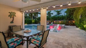 An outdoor patio with a glass table and chairs, a pool, and a view of the surrounding greenery. - Amazing private pool-spa home just blocks from the beach.  (Naples)