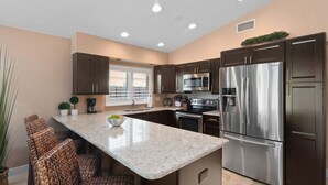A modern kitchen with dark cabinets, stainless steel appliances, and a central island with seating. - Amazing private pool-spa home just blocks from the beach.  (Naples)