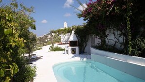 A pool area with a white pool, a small structure with bottles, and lush greenery. - Domes, flowers and a small, cool pool (Le Forna)