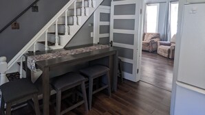 Une cuisine moderne avec un plancher en bois foncé, un escalier blanc et un coin repas agrémenté d’une nappe à motifs.