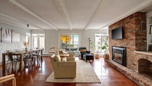Een ruime woonkamer met een open haard, een eethoek met een grote tafel en stoelen, en een gezellige zithoek met banken en een vloerkleed.