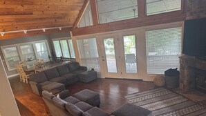 Ein geräumiges Wohnzimmer mit einem großzügigen Ecksofa, einem Kamin und großen Fenstern mit Jalousien.