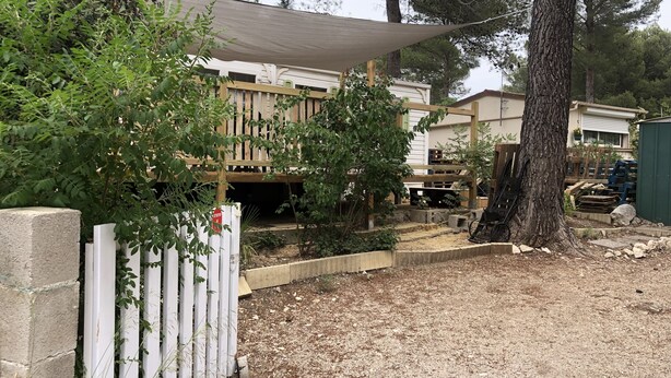 A fenced outdoor area with a wooden deck, a shaded area, and a tree. - Mobile home 32 m2. Sleeps 4. In a secure residence (Le Castellet)