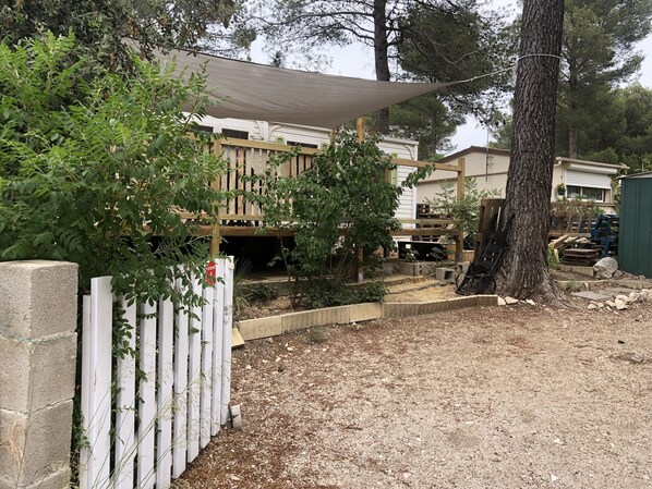 Un espacio exterior cercado con una terraza de madera, una zona sombreada y un árbol.