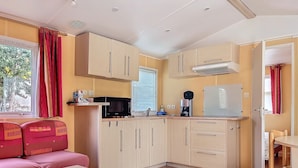 A compact kitchen with a microwave, coffee maker, and a refrigerator. There is a small dining area with a table and chairs. - Mobile home 32 m2. Sleeps 4. In a secure residence (Le Castellet)