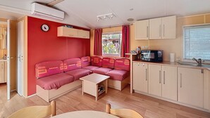 A compact living space with a kitchenette, a sofa, a dining table, and a clock on the wall. - Mobile home 32 m2. Sleeps 4. In a secure residence (Le Castellet)