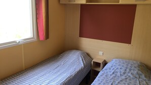 A small, single-bed room with a window, a wooden cabinet above the bed, and a small table beside the bed. - Mobile home 32 m2. Sleeps 4. In a secure residence (Le Castellet)