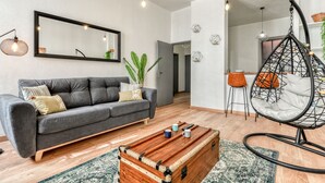 Ein modernes Wohnzimmer mit einem grauen Sofa, einer Holzbank, einem Hängekorbstuhl und einem Essbereich im Hintergrund.
