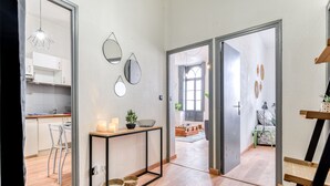 Eine moderne Küche mit weißen Schränken, ein Essbereich mit Tisch und Stühlen sowie ein Flur, der in ein Wohnzimmer mit Sofa und Couchtisch führt.