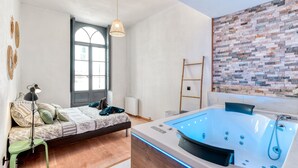 Ein Schlafzimmer mit Bett, Nachttisch, Lampe und einer großen Badewanne mit Bedienelementen.