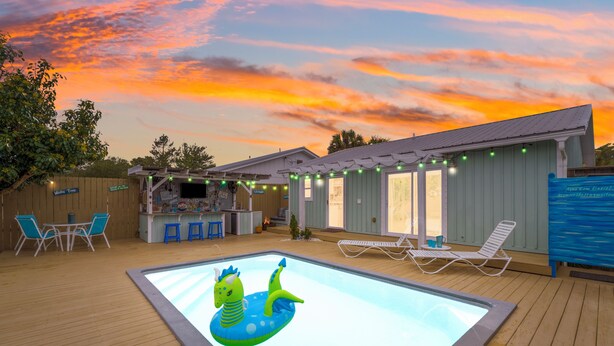 Ein Garten mit Pool, Luftmatratze, Bar im Freien und Liegestühlen.