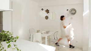 Ein moderner, minimalistischer Essbereich mit einem weißen Tisch, Stühlen und einem Blumentopf.