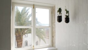 Ein Badezimmer mit Fensterblick auf Palmen, einer weißen Fliesenwand und zwei hängenden Pflanzgefäßen.