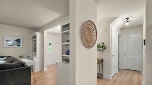 A modern living room with a gray sofa, a white dining table, and a kitchen area with white cabinets and shelves.