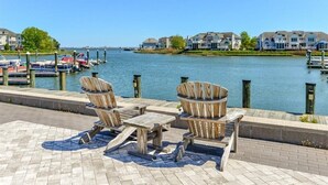 A waterfront patio with wooden furniture and a view of houses across the water.