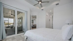 Un dormitorio con una cama grande, un ventilador de techo y un ventanal corredero que da a un balcón con mobiliario exterior.