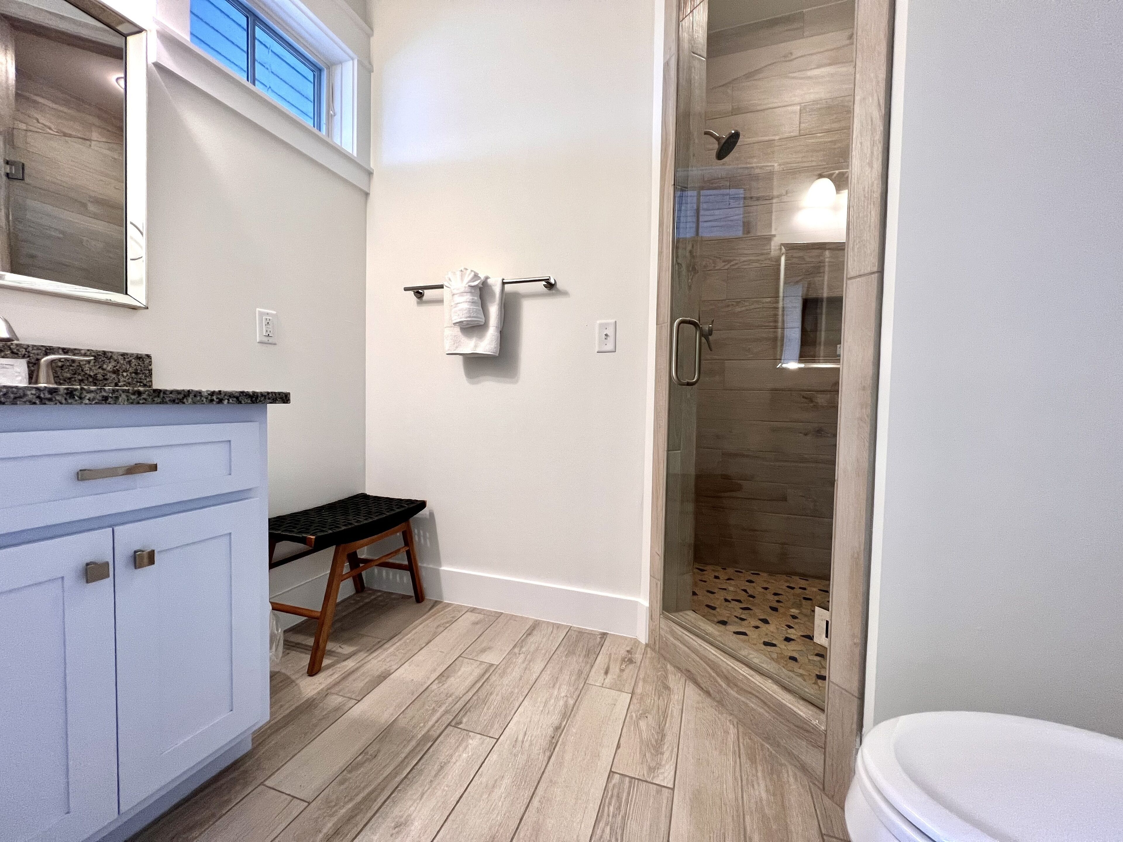 Un baño moderno con ducha, tocador con encimera y un banco de madera.