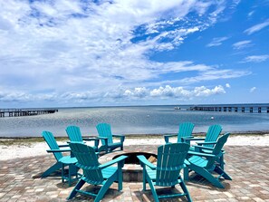 A beachside seating area with turquoise Adirondack chairs facing a calm sea and a pier in the distance. - Bay side home in a lovely, gated community, beach gear, pools, hot tub! (Port Saint Joe)