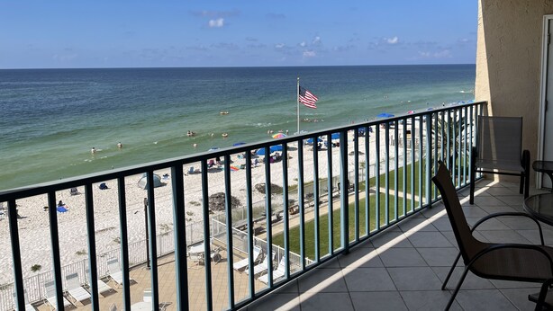 A balcony with a view of the beach, a flag, and outdoor seating. - Surf Side Shores 2405  2 bd 2 ba  gulf-front  (Gulf Shores)