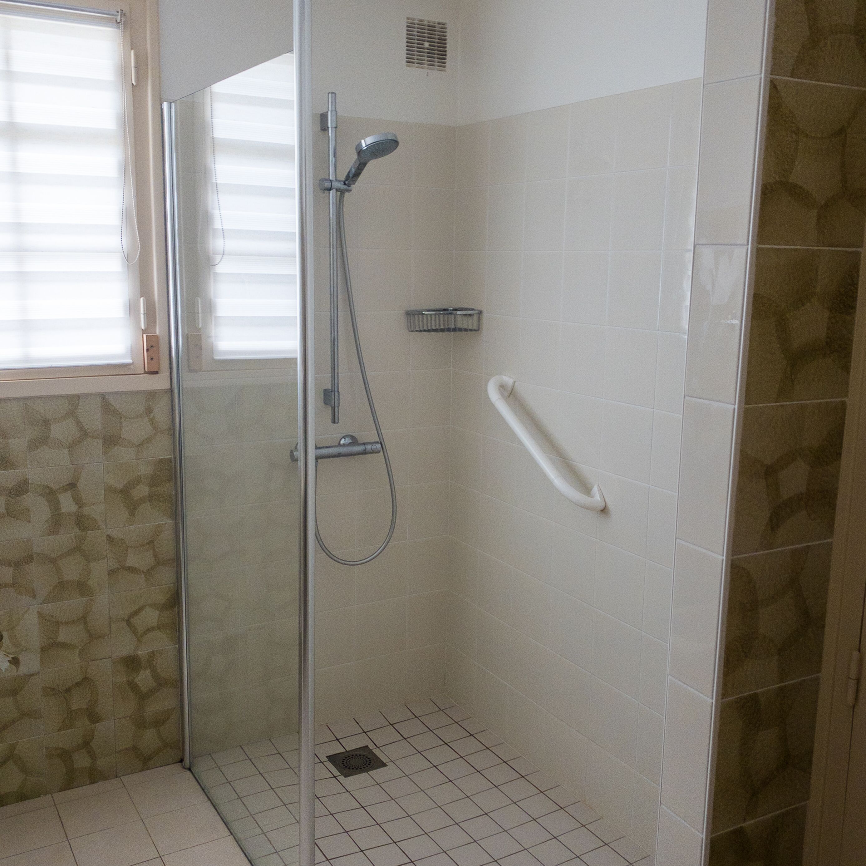 A glass-enclosed shower with a handheld showerhead and a wall-mounted faucet.