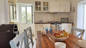 Een moderne keuken met witte kasten, een houten eettafel met een fruitschaal, en een barbecue buiten.