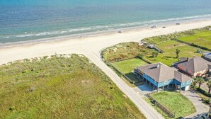 Vista aérea de uma área residencial costeira com casas, uma praia e uma estrada que leva à praia.