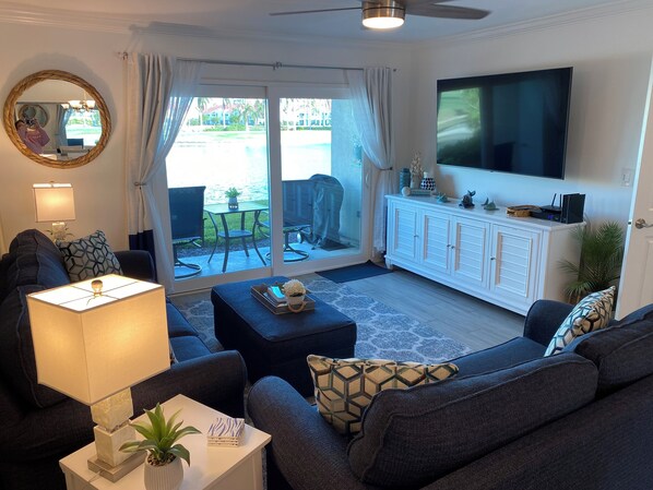 A living room with a sofa, a coffee table, a TV, and a sliding glass door leading to an outdoor area with a pool.