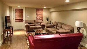 Un salon avec deux canapés, dont un rouge, une table basse, un téléviseur posé sur un meuble et une lampe.