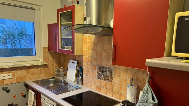 A compact kitchen with a stove, sink, and a microwave. There is a window providing a view of the outside.
