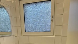 A small, clean bathroom with a white sink, a toilet, and a window.
