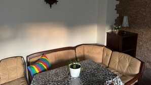 A corner seating area with a cushioned bench, a table with a patterned tablecloth, a potted plant, and a wall-mounted clock.
