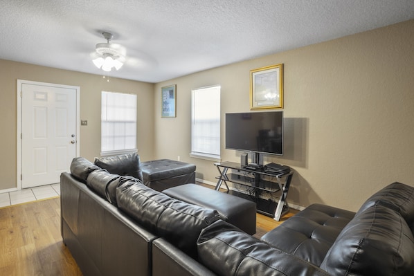 A living room with a black leather sofa, a TV on a stand, and a ceiling fan.